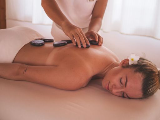 A woman receiving a hot stone massage at a spa, with a flower in her hair, creating a relaxing and serene atmosphere.