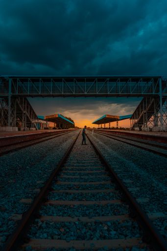A vertical shot of railway tracks and a pedestrian steel bridge during sunset