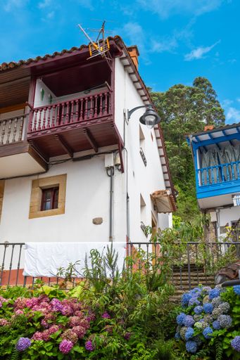 A charming house with a wooden balcony and colorful flowers in front on a sunny day. Tazones, Spain