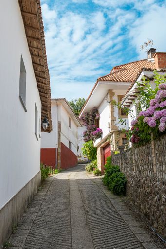 A charming narrow street in Tazones with white houses and colorful flowers under a blue sky. Spain