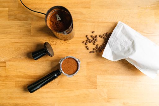 Top view of coffee making essentials including grinder, tamper, and coffee beans on a wooden surface