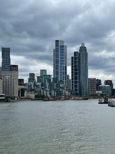 A scene of Modern skyscrapers along the Thames River in London under a cloudy sky