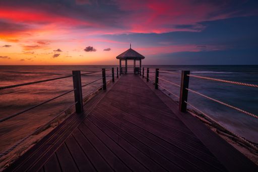 A scenic view of a pier extending into the ocean at sunset with a vibrant sky in Montego Bay, Jamaica