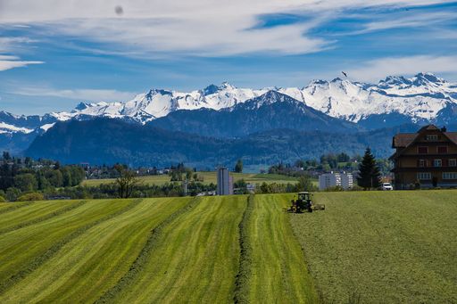 A Beautiful scenery of a tractor in the green land with icy mountains under cloudy blue sky on a summer day