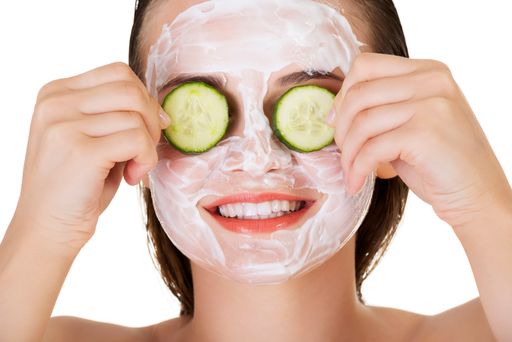 A beautiful woman with a facial mask putting cucumber slices on her eyes
