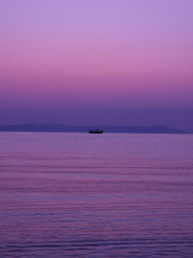 A serene view of a boat on a calm sea during a purple sunrise with distant mountains in the background