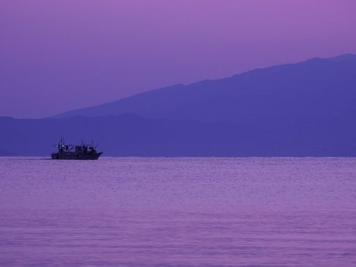 A serene view of a boat floating on the calm sea during a purple sunrise