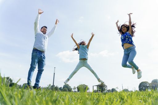 A cheerful Hispanic family jumping in a park covered in greenery on a sunny day