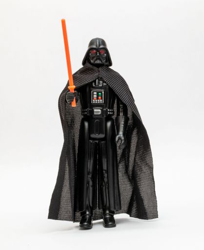 A close-up of a Darth Vader action figure holding an orange lightsaber isolated on a white background
