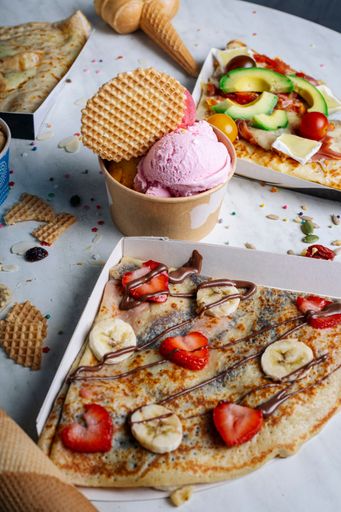 A vertical closeup shot of crepes with different toppings and a bowl of ice cream