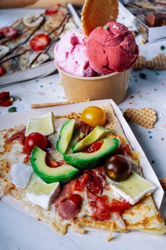 A vertical shot of a crepe with savory toppings and a bowl of ice cream