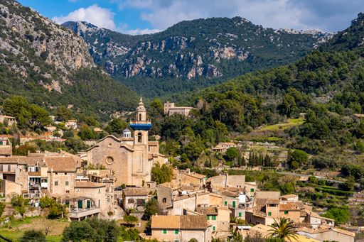 A View of Carthusian Monastery Valldemossa with green mountains under blue cloudy sky in valldemossa, Mallorca, Spain