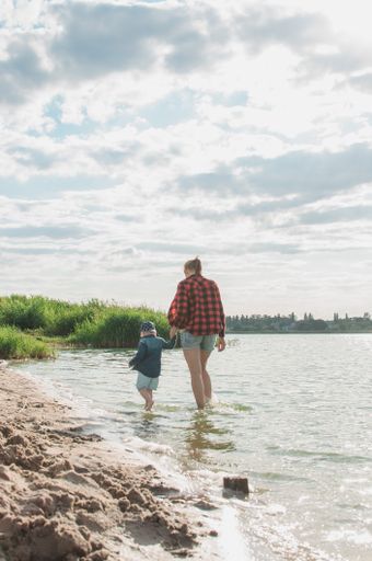 A vertical shot of a woman and her child walking on a beac