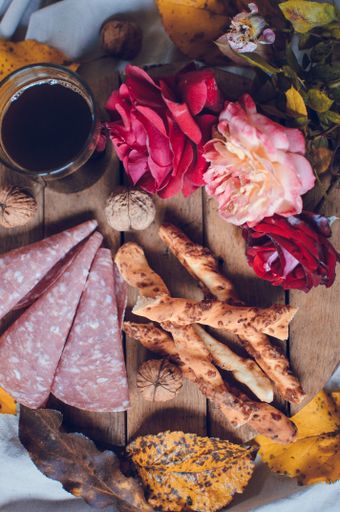 A vertical shot of salami, breadsticks, a glass of wine and leaves on a wooden tray