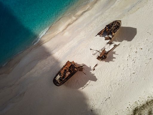 Aerial view of two shipwrecks on a sandy beach with clear turquoise water.