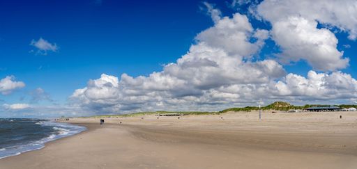 A vast, sandy beach stretches out towards a horizon dotted with low green hills and a sky filled with fluffy clouds.