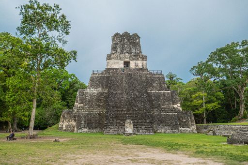 A view of the ancient Mayan Temple I in Tikal, Guatemala, surrounded by lush greenery and under a clear sky.