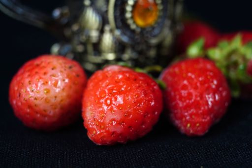 A closeup of ripe delicious strawberries and a vintage metal cup isolated on a black background