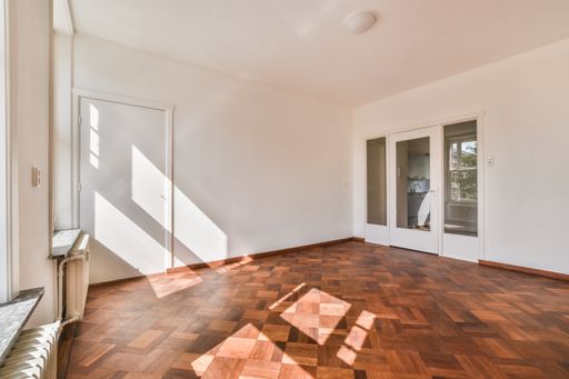 An empty room with white walls and a wooden floor.