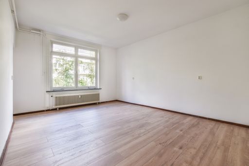An empty room with white walls, windows, and a wooden floor.