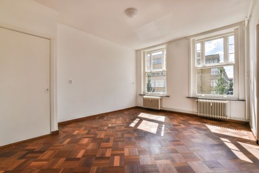 An empty room with white walls, windows, and a wooden floor.