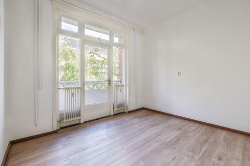 An empty room with white walls, a wooden floor, and a balcony.