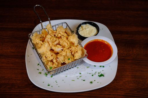 A white plate of crispy chicken popcorn served with a side of ketchup and mayonnaise on a wooden table