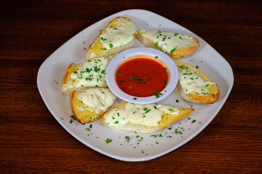 A closeup of a freshly baked garlic bread topped with melted cheese and served with tomato sauce on a wooden table