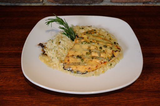 A closeup shot of a chicken breast served with rice and pepper sauce on a white plate on a wooden table
