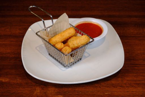 A closeup shot of tasty Mozzarella sticks served with ketchup on a white plate on a cafe table