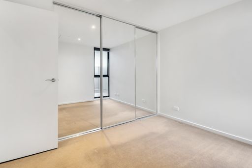 A corner of an empty room with white walls and a wardrobe with mirror sliding doors