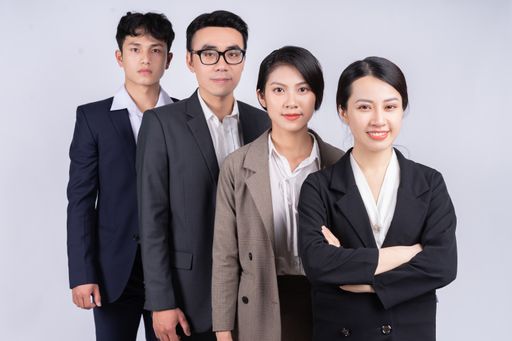 A young Vietnamese business team in suits happily posing on background of a white wall