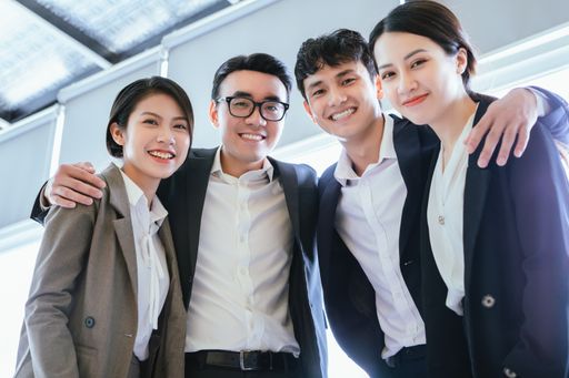 A young Vietnamese business team in suits hugging each other in the office
