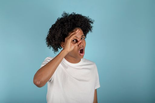 A funny Latino guy with afro hair and a shocked expression holding his hand to his eye like a monocle