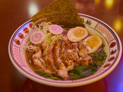 A mouth-watering bowl of Japanese ramen with sliced meat, boiled egg, narutomaki, and seaweed served in a traditional bowl on a wooden table.