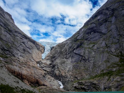 A beautiful landscape featuring a glacier nestled between rugged mountains under a partly cloudy sky.