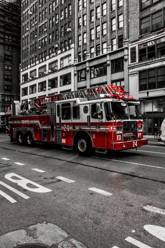 A vibrant red fire truck from FDNY driving through the streets of New York City with tall buildings in the background