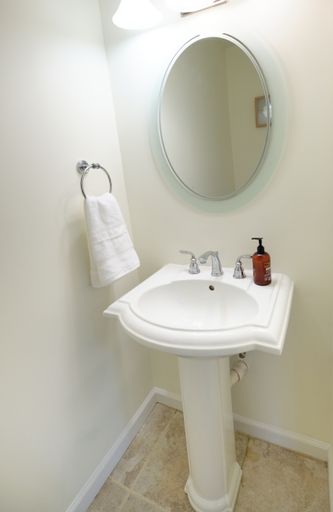 A vertical shot of a bathroom sink with liquid hand soap, mirror, and a white towel hanging on a metal towel ring