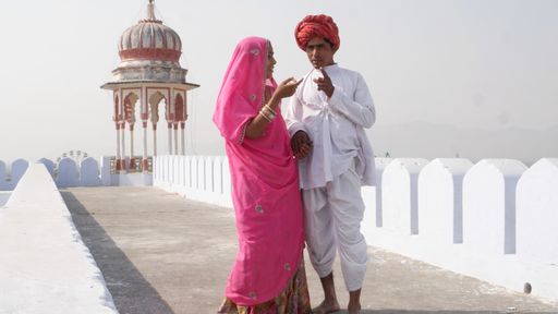 Two Indian male and female dressed in national clothing standing in front of an interesting building