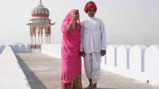 An Indian couple in traditional outfits holding hands with a temple in the background.