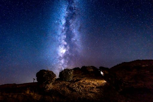 A stunning view of the Milky Way galaxy over rocky terrain at night with a clear starry sky.