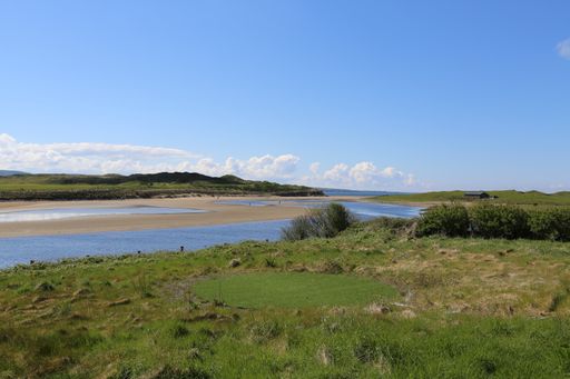 A beautiful view of a flowing river surrounded by greens gleaming under the cloudy blue sky