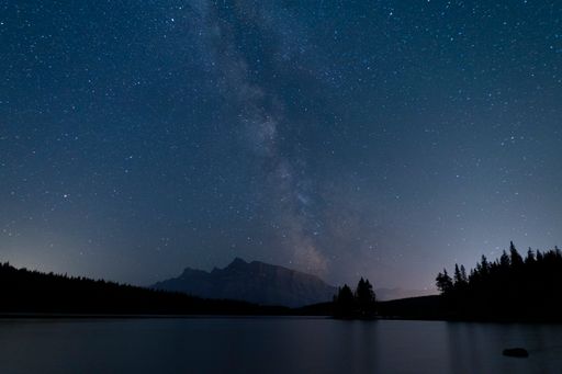 A beautiful nightscape featuring the Milky Way galaxy arcing across the sky with the reflection of starlight shimmering on a tranquil lake below