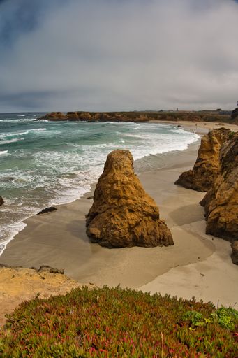 A beautiful view of the wavy sea hitting the sandy beach surrounded by rocky cliffs on the coast