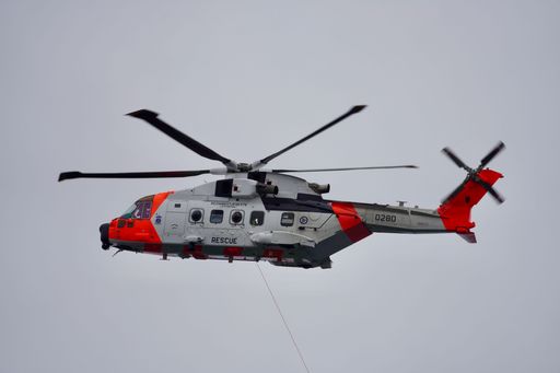 A rescue helicopter in flight with a clear sky background, showcasing emergency services in action.