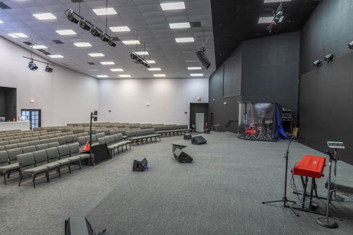 Interior of a modern auditorium with rows of seats, stage, musical instruments, and lighting equipment.