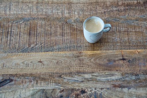 A top view closeup of a mug with a heart carved on it with coffee placed on a wooden table