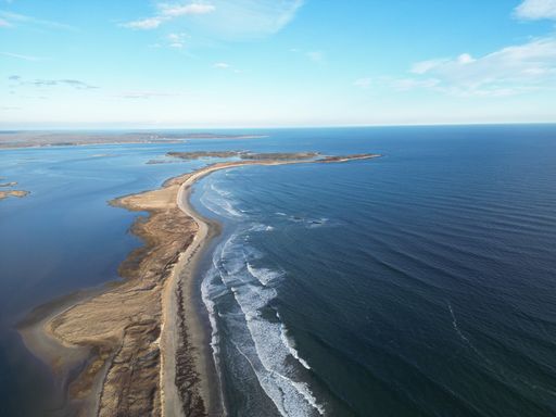 Aerial view of a coastal landscape with a long sandy beach and clear blue ocean under a bright sky.
