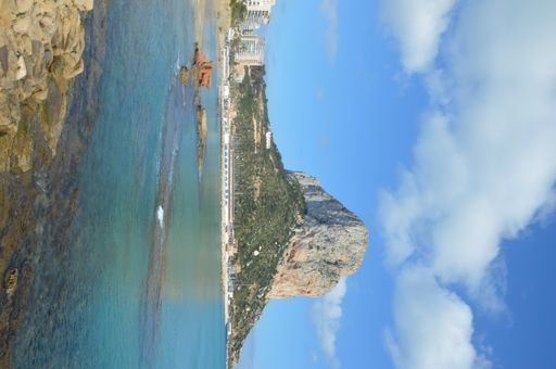A vertical shot of a cliff against the cloudy sky in Calpem Spain
