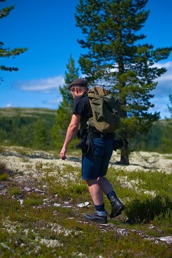 A vertical shot of a Caucasian man hiking on a rocky hill with a backpack in Norway